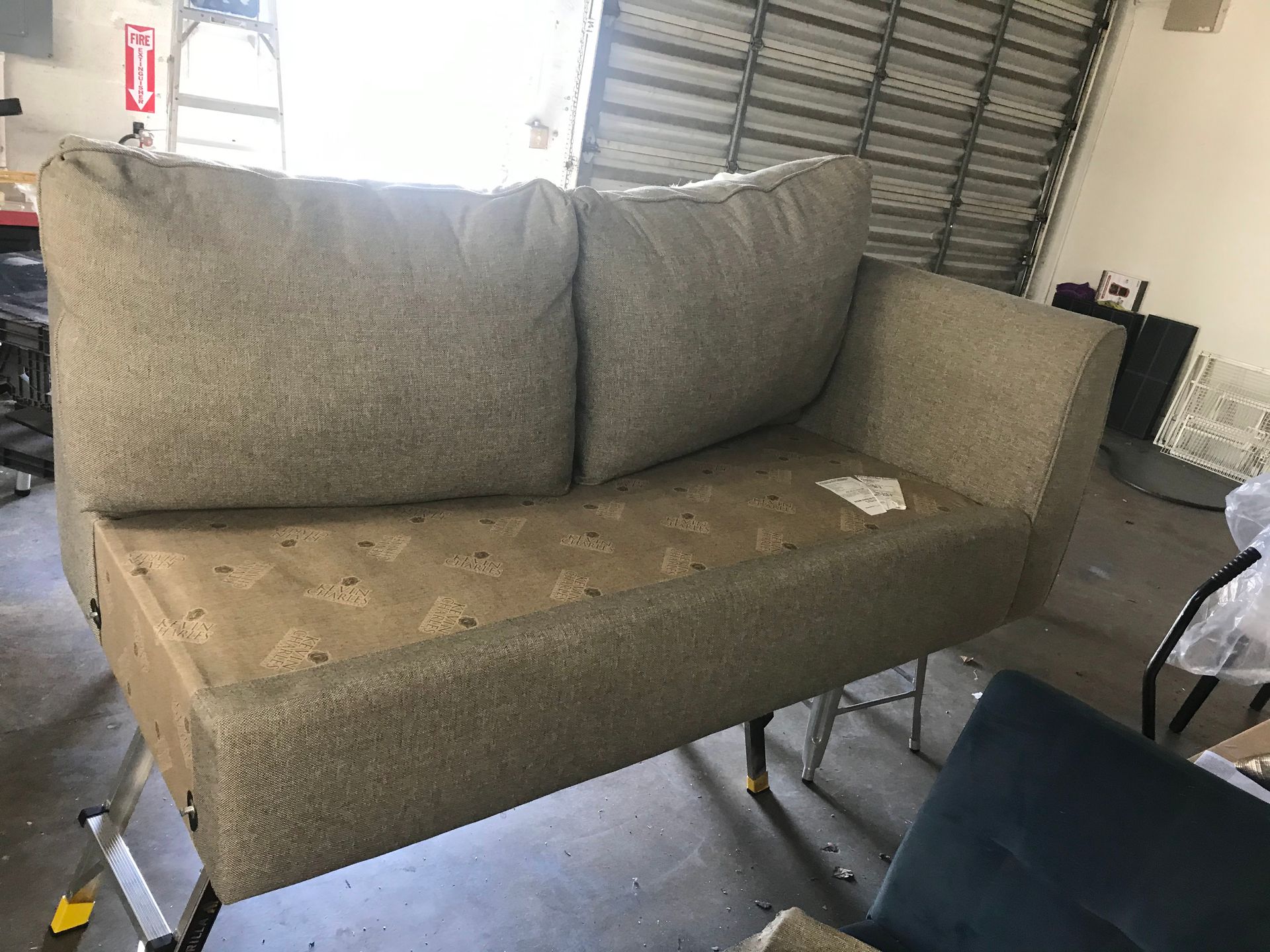 Tan loveseat with two large back pillows, in a garage setting.