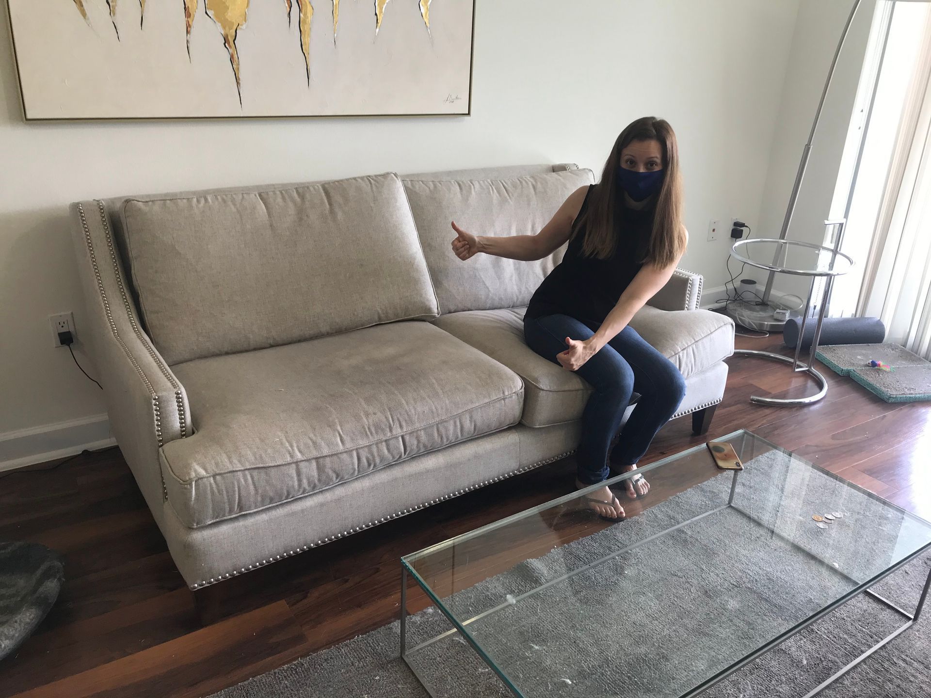 A woman wearing a mask is sitting on a couch giving a thumbs up