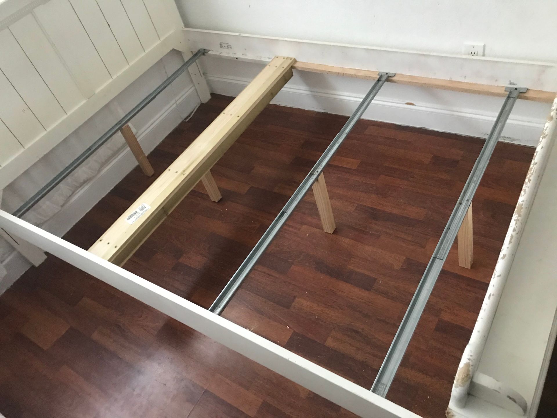A white bed frame is sitting on a wooden floor