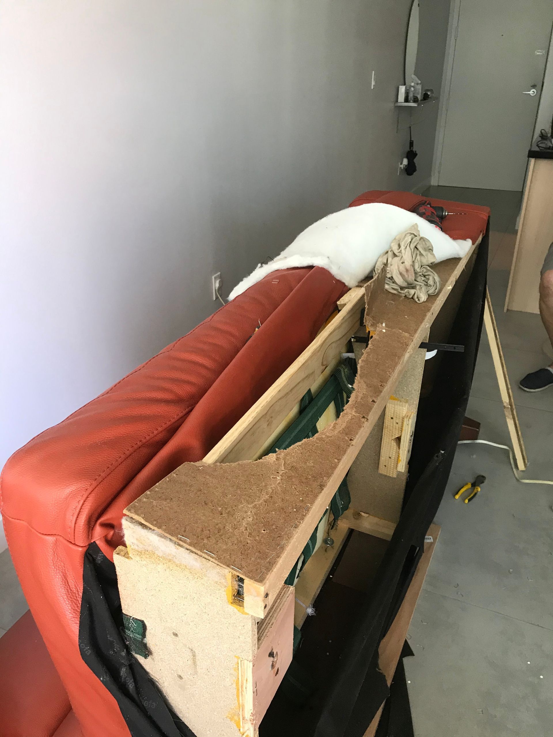 A red leather couch is being dismantled in a garage.
