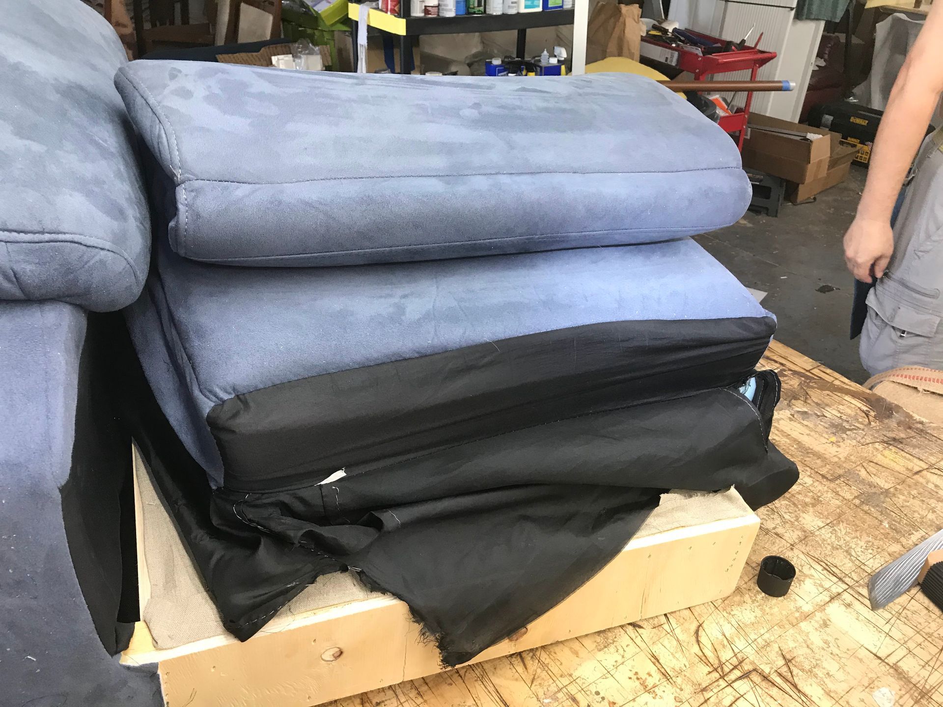 A person is standing next to a pile of cushions on a wooden table.
