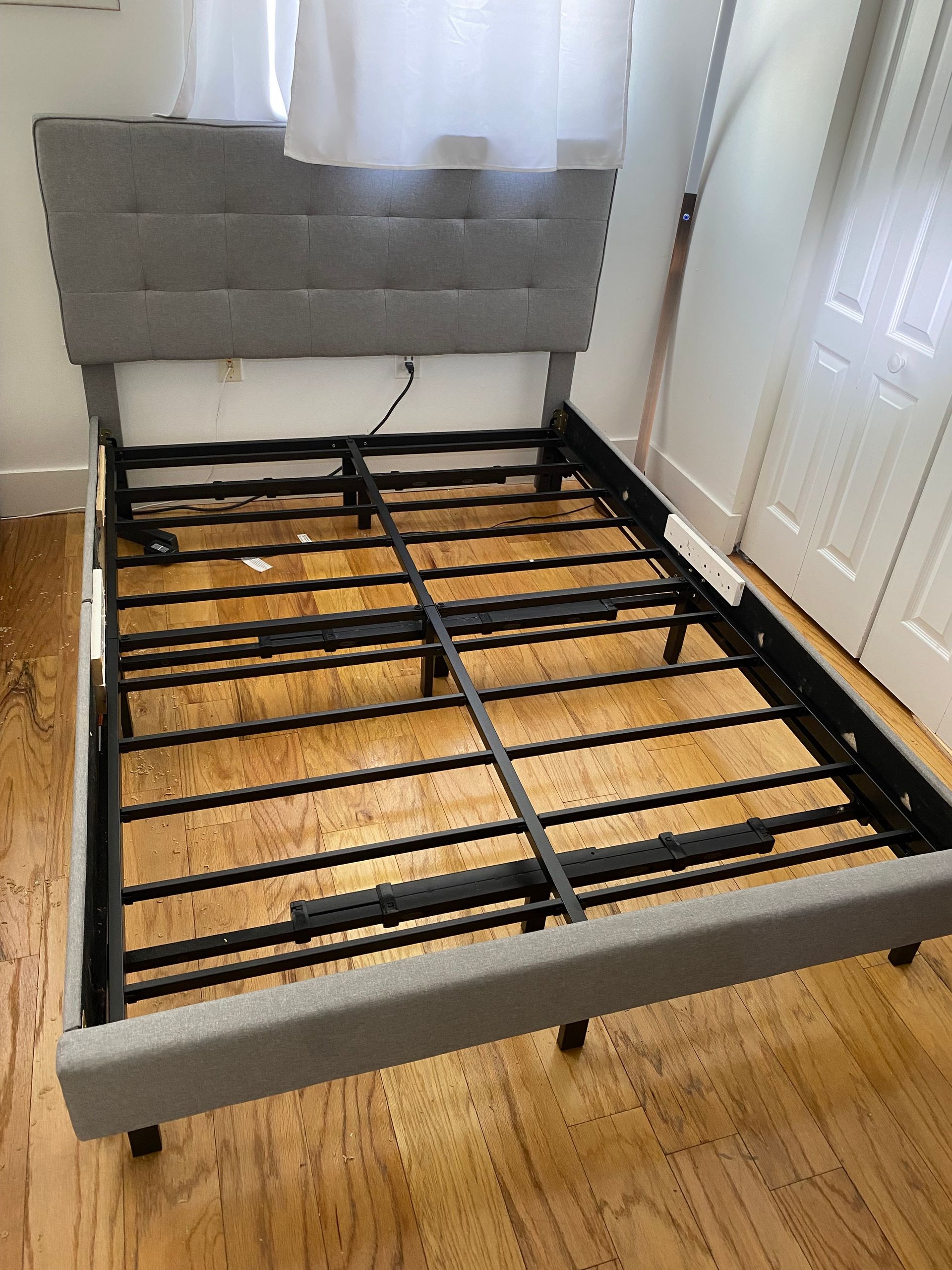 A bed frame is sitting on a wooden floor in a room.