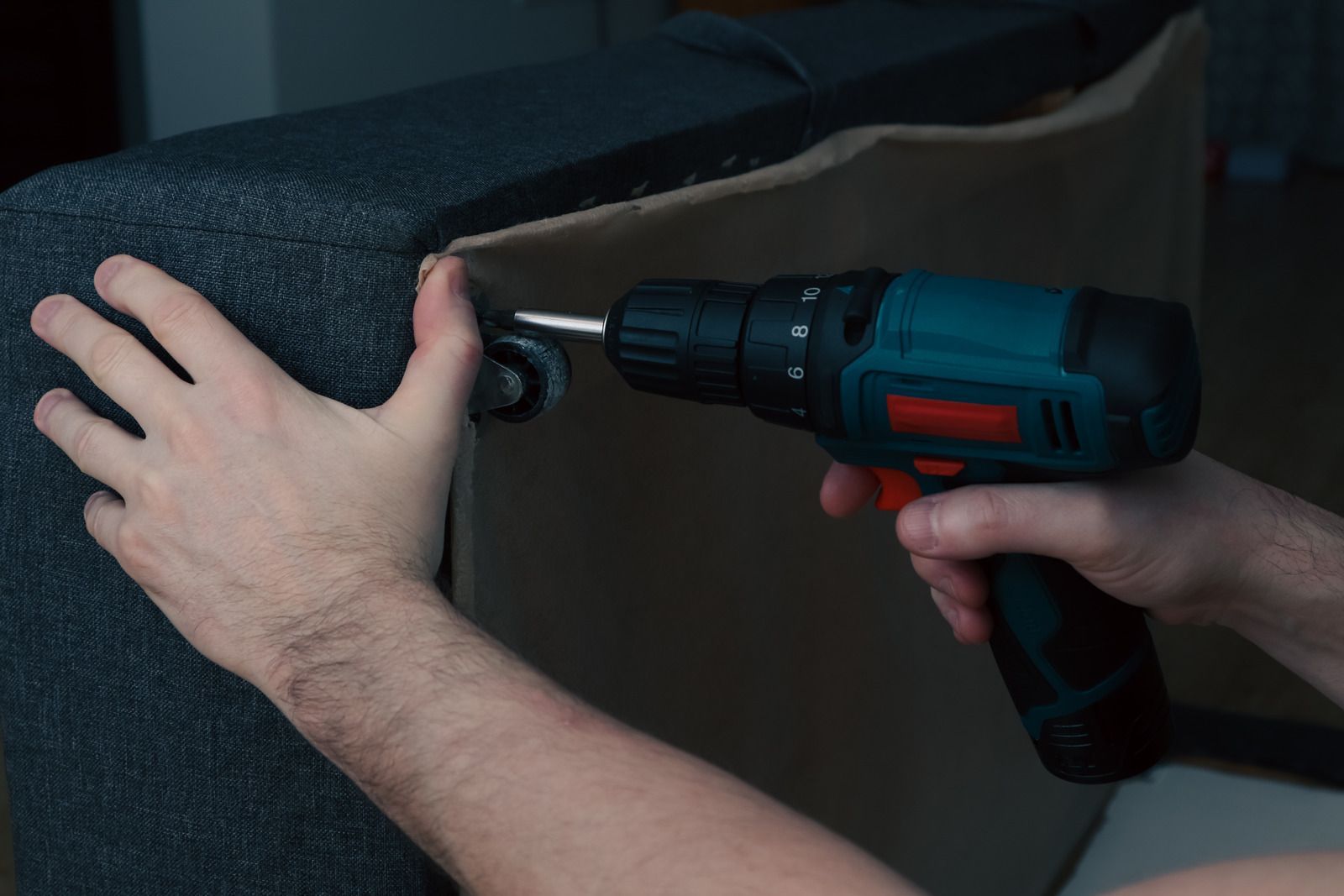 A person is using a drill to fix a couch.
