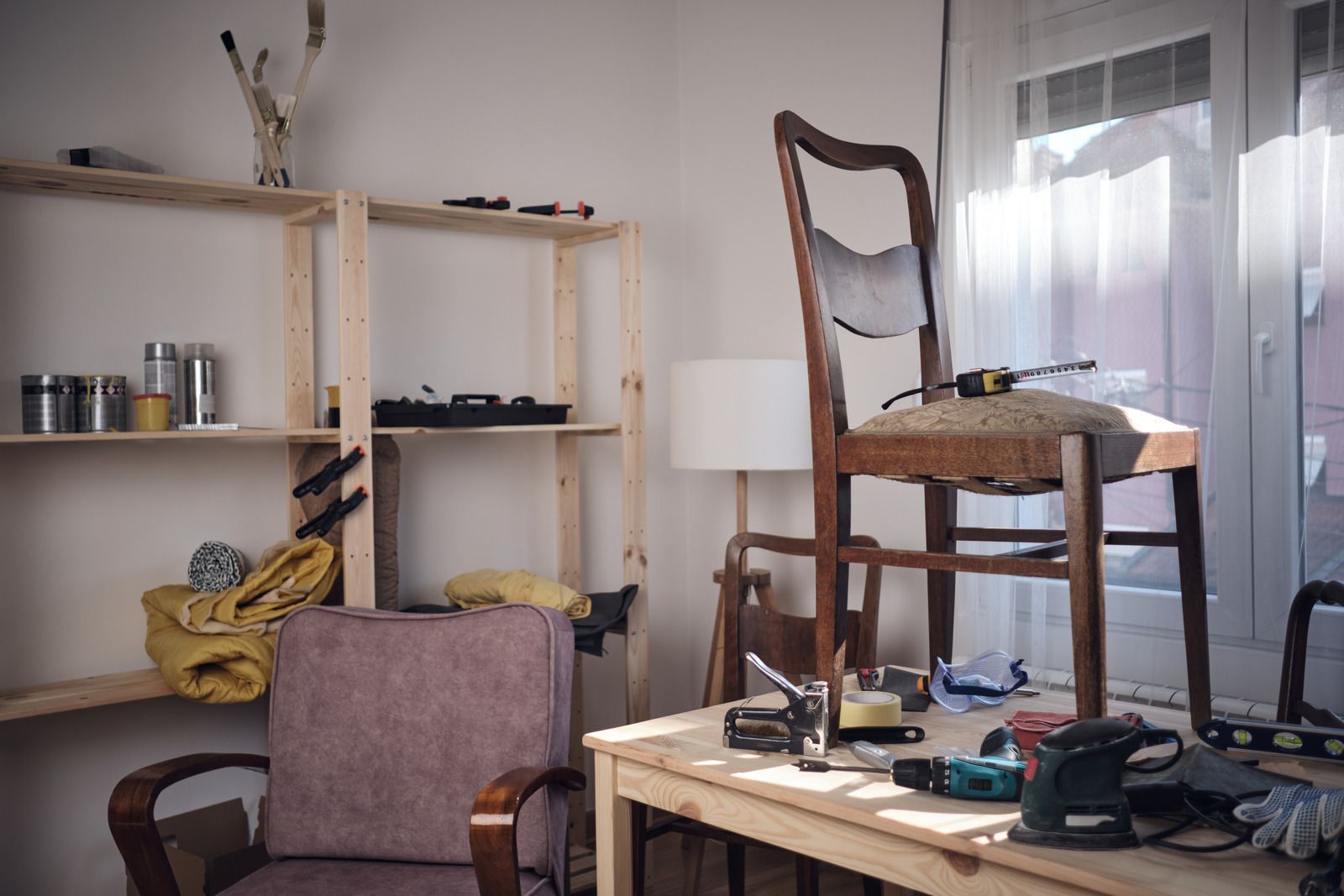 Workshop scene with antique chair being reupholstered. Tools on table.