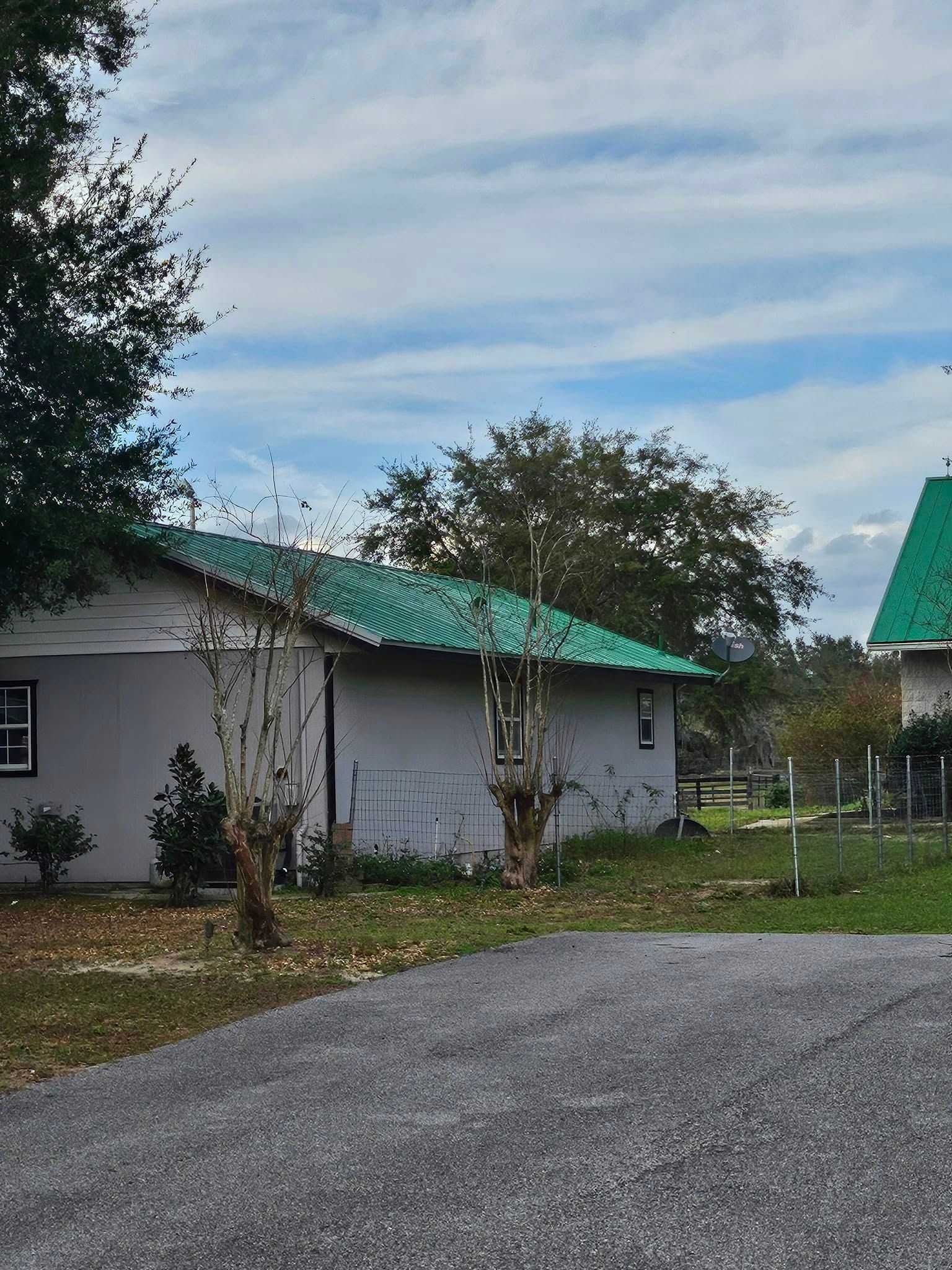 A white house with a green roof is surrounded by grass and trees