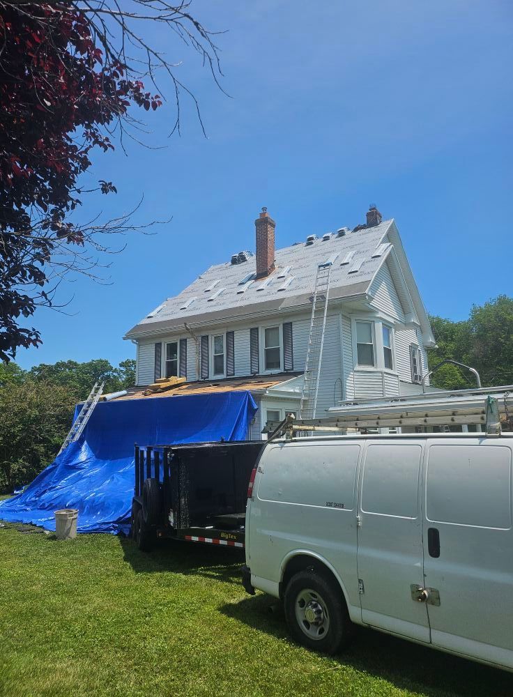 A white van is parked in front of a house with a tarp on the roof.