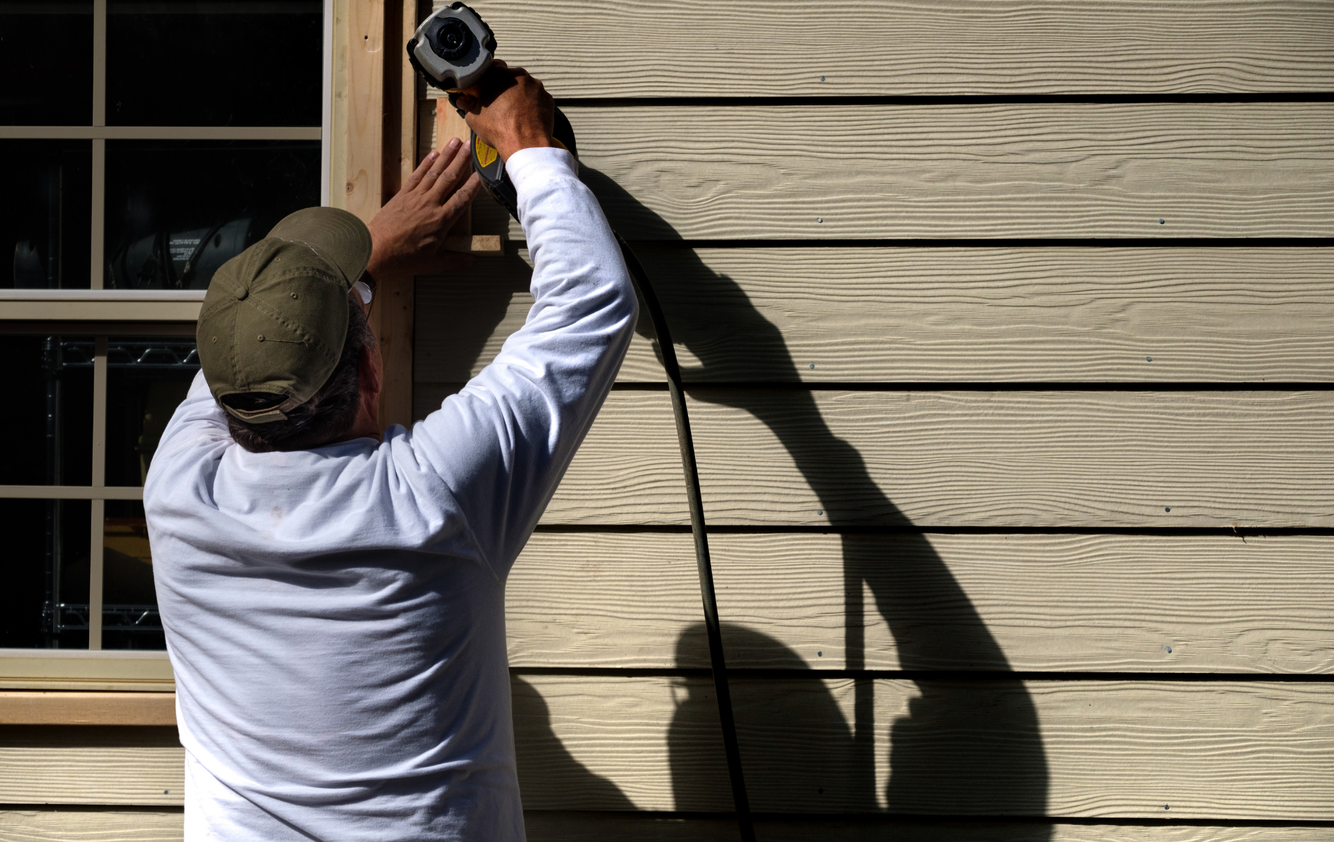A man is installing a window on the side of a house.