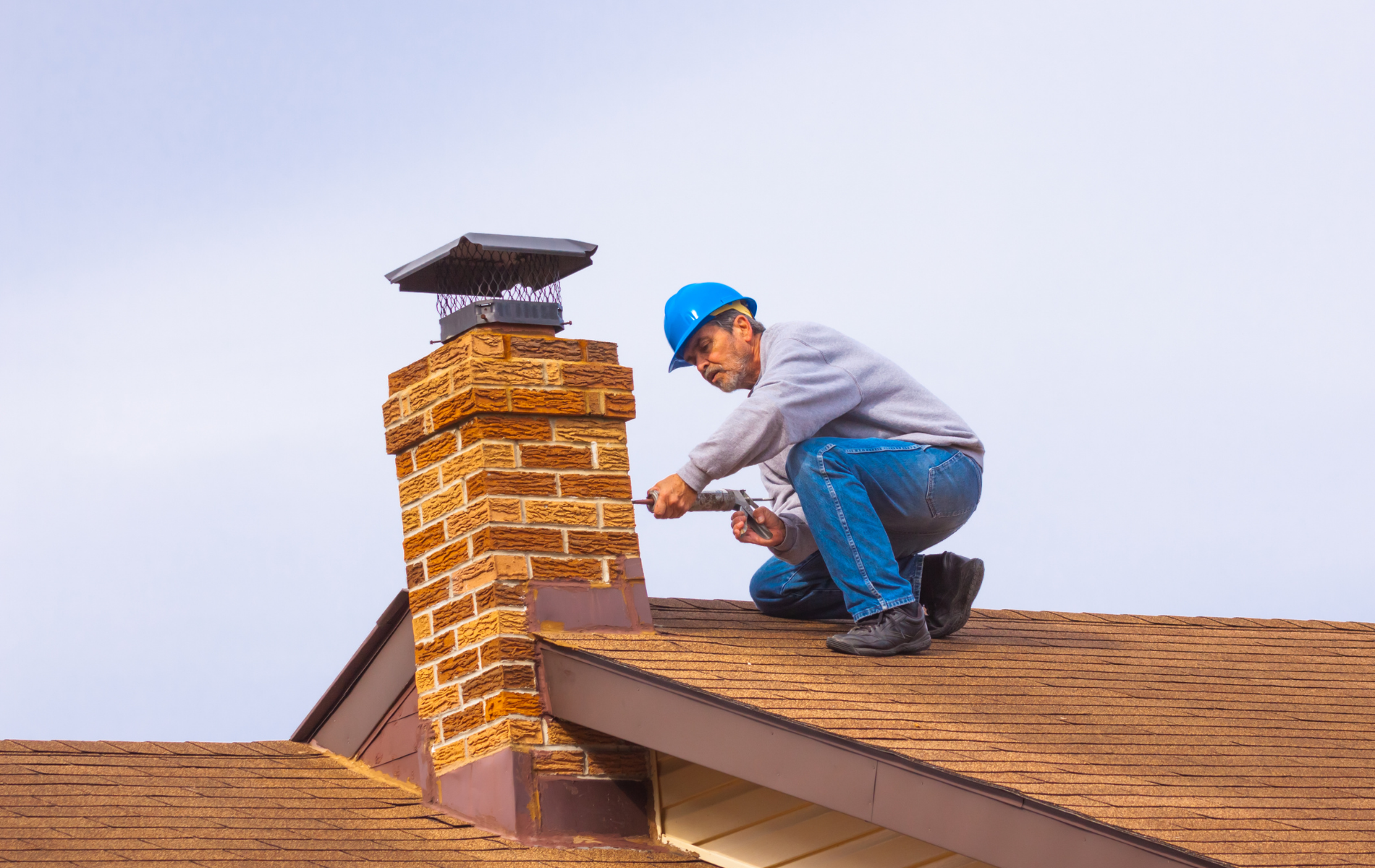 A man is kneeling on top of a roof fixing a chimney.