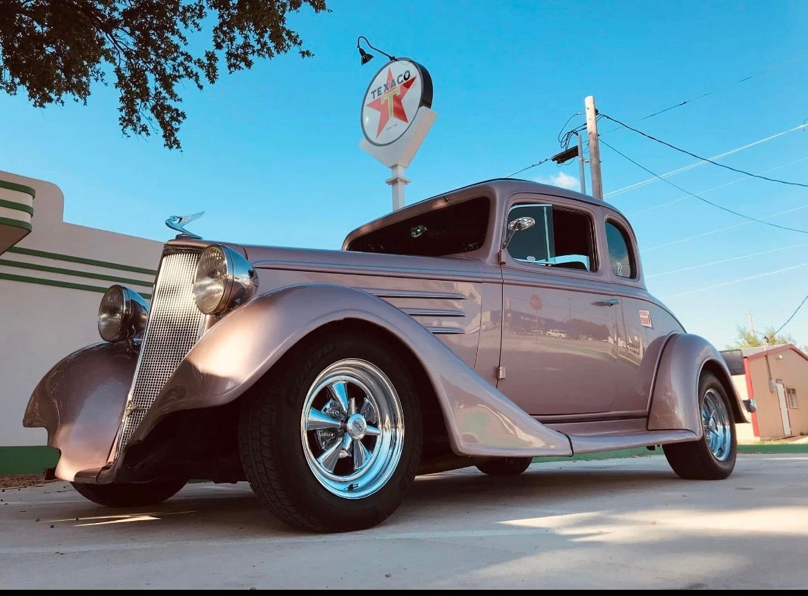 An old fashioned car is parked in front of a gas station