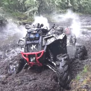 A person is driving a four wheeler through a muddy area.