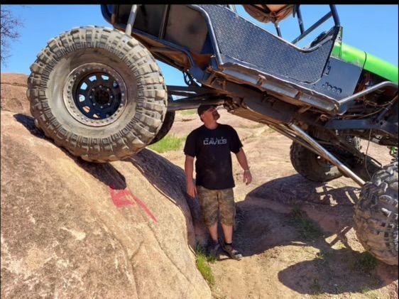 A man in a black shirt stands next to a monster truck