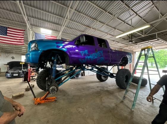 A purple truck is sitting on a lift in a garage.