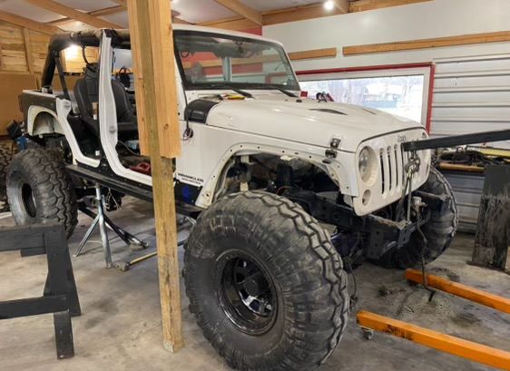 A white jeep is sitting on a lift in a garage.