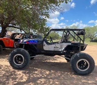 A jeep is parked next to another jeep in a dirt field.