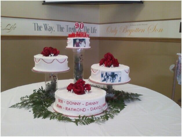 Four tiered cakes with red roses and photos, for a 90th birthday celebration on a table.