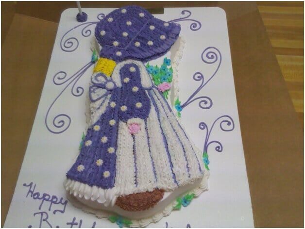 Girl-shaped cake with purple hat, dress, and white frosting. 