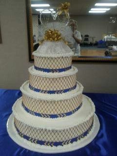 Four-tiered wedding cake with blue and gold lattice design, topped with gold embellishments, on a blue tablecloth.
