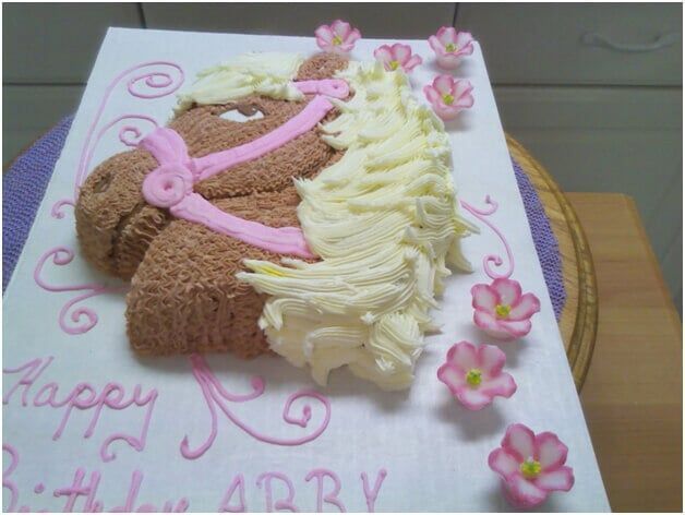 Horse-shaped birthday cake decorated with pink frosting and flowers, with 