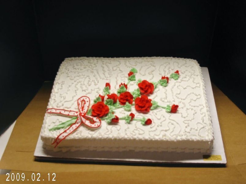 Square white cake decorated with red roses, green leaves, and a ribbon.
