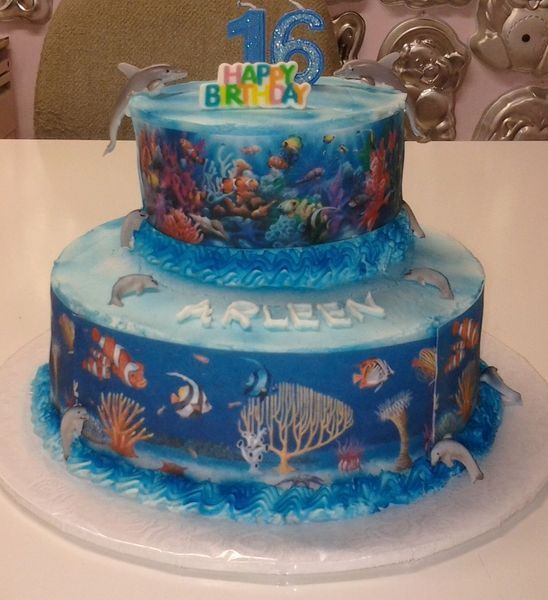 Two-tiered birthday cake with an underwater theme; dolphins, coral, and fish; blue and colorful.