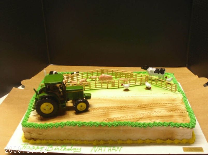 Birthday cake decorated with a tractor, farm animals, and a field, with green and yellow frosting.