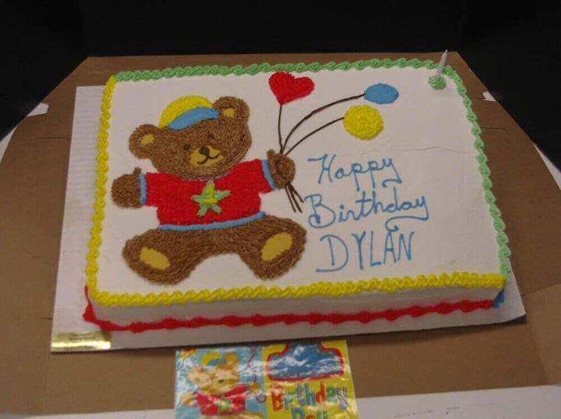 Birthday cake with a teddy bear holding balloons. 