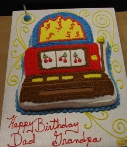 Birthday cake decorated as a slot machine with cherries, dollar signs, and text: 