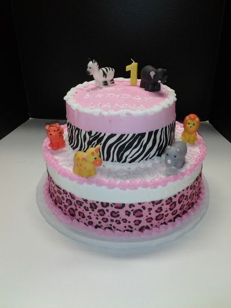 Two-tiered birthday cake with animal decorations and pink and zebra print frosting.