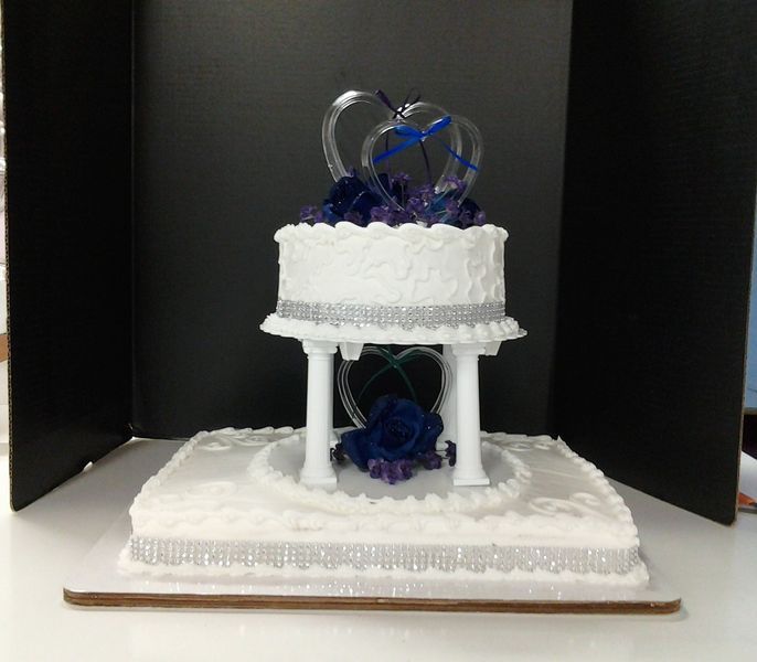 Two-tiered white wedding cake with blue and silver decorations and heart-shaped toppers.