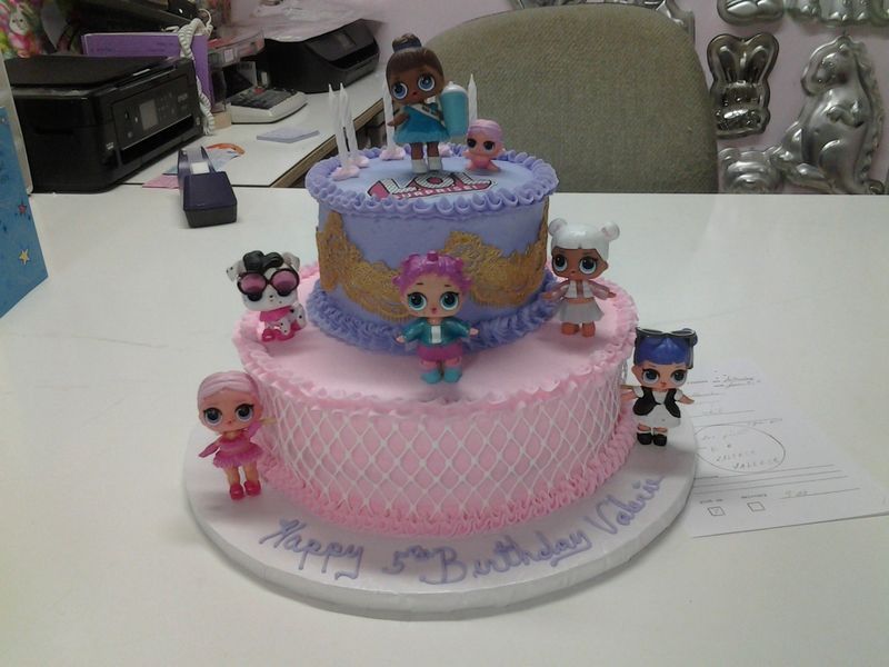 Two-tiered pink and purple cake decorated with LOL Surprise dolls, candles, and 