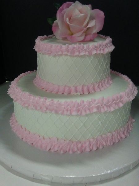 Two-tiered cake with pink frosting ruffles and a pink rose on top, white frosting with a lattice design.