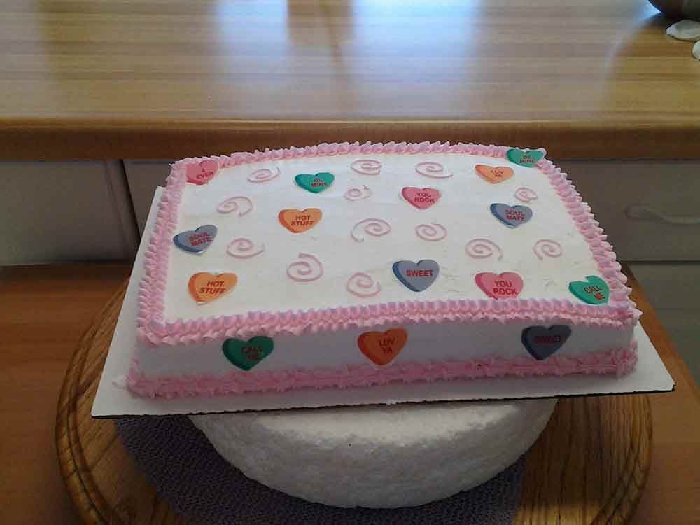 A rectangular cake decorated with pink frosting, hearts, and swirls, sitting on a round platform.