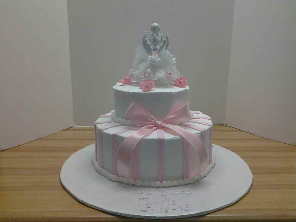 Two-tiered white cake with pink ribbon and flowers, topped with a decorative figure.