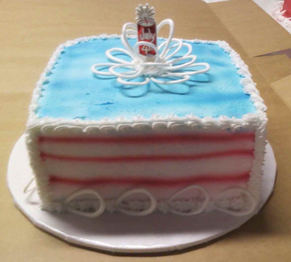 Square cake with blue frosting and red stripes; topped with a decorative flower and a small bottle.