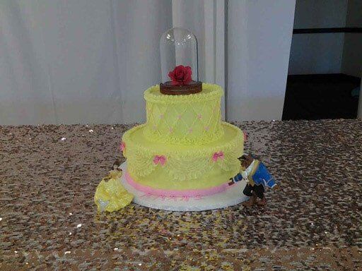 Cake decorated like Beauty and the Beast; yellow, pink, and white with figures and a rose.