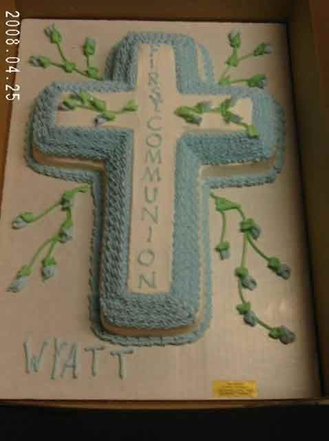 A cross-shaped cake decorated with blue frosting and vines, inscribed 
