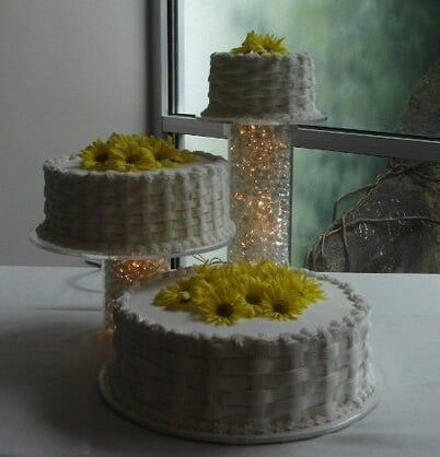 Three-tiered white cakes decorated with yellow flowers, set on stands, by a window.