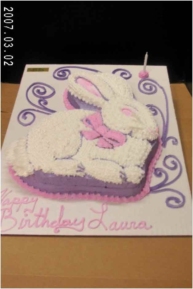 Birthday cake shaped like a white rabbit with a pink bow and purple accents, text says 
