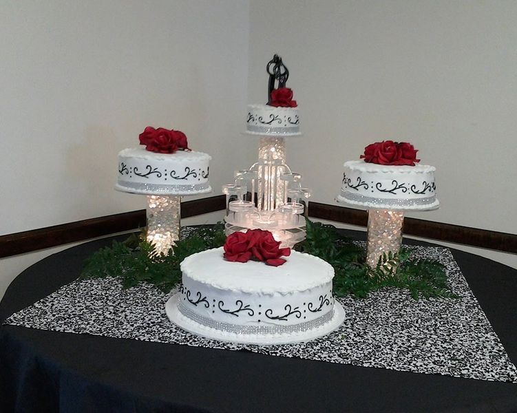 Wedding cakes on tiered stands, decorated with red roses and silver accents, on a table.