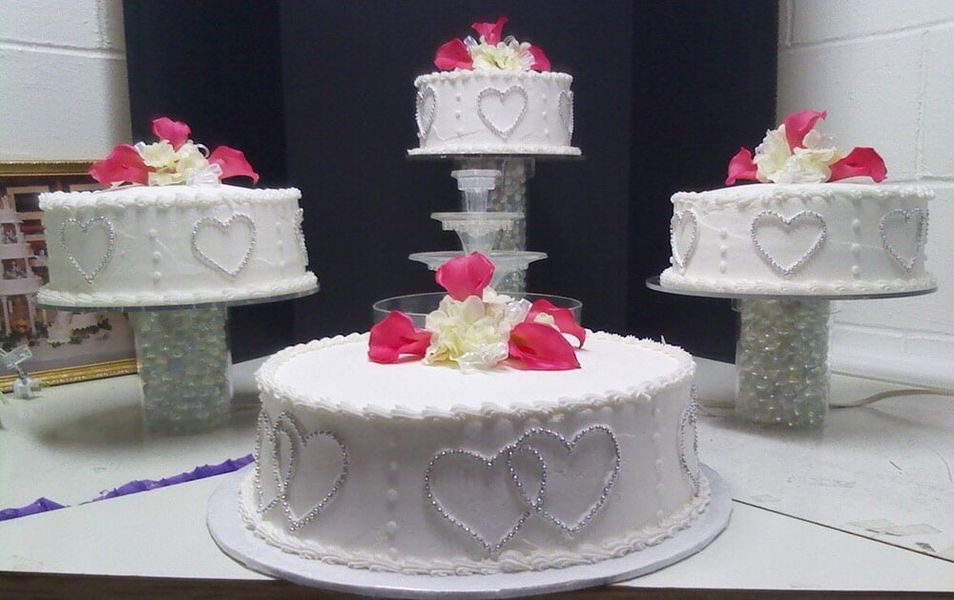 Wedding cake display: White cakes decorated with hearts and flower petals on clear stands.