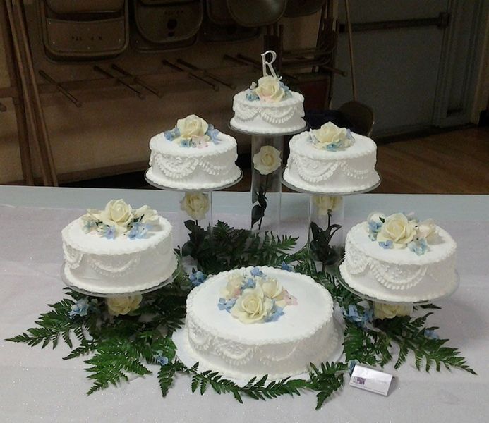 Wedding cake display with multiple tiers, decorated with white frosting and roses, on a white tablecloth.