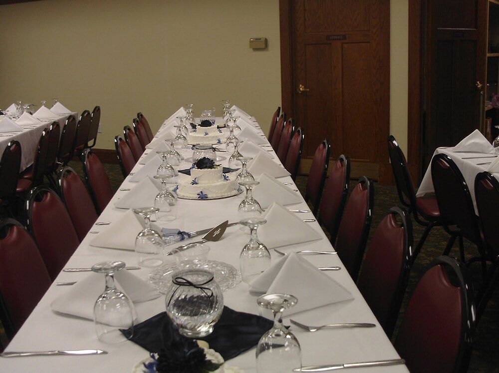 Long banquet table set for a formal event with white linens, chairs, and glasses.