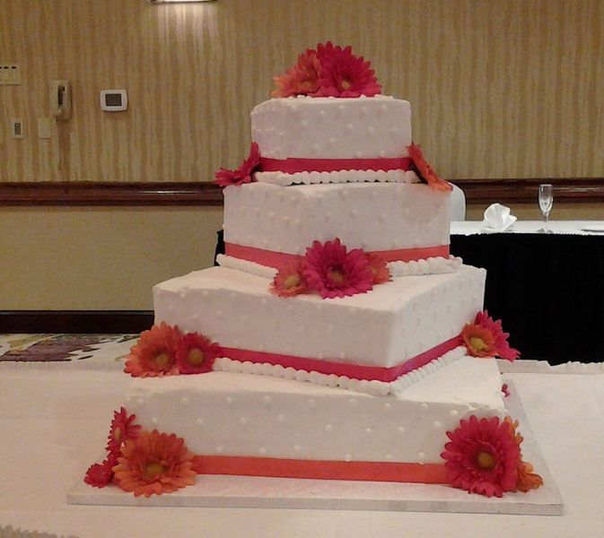 Four-tiered white square cake with pink ribbon and orange flowers.