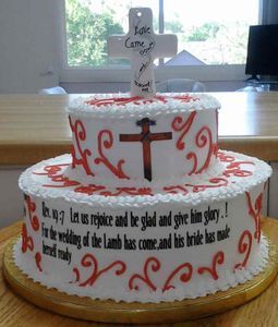 Two-tiered wedding cake with red accents, a cross topper, and Bible verse.
