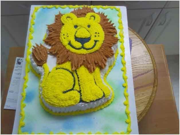 Lion-shaped cake with yellow body and mane, brown fur, on a rectangular cake with a blue-green background.