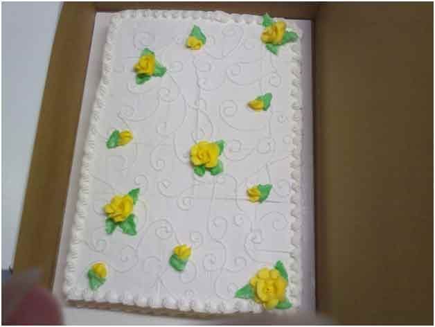 Rectangular white frosted cake in a box, decorated with yellow roses and green leaves.