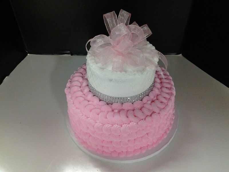 Two-tiered pink and white cake with bow and rhinestone trim on a white plate.