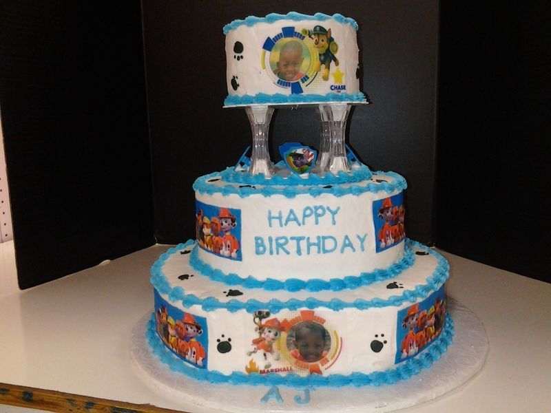 Three-tiered Paw Patrol birthday cake with blue frosting and character images.