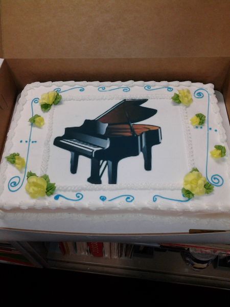 Cake decorated with a grand piano design, surrounded by yellow flowers and blue accents.