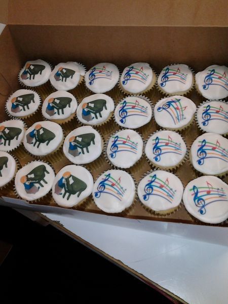 Cupcakes in a box. Some feature a piano player, others music notes.